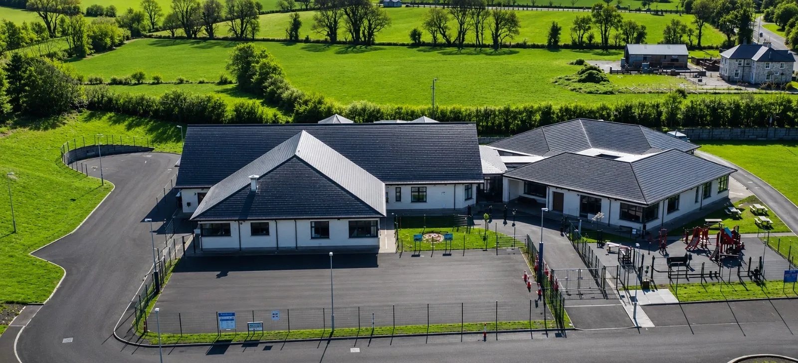 Aerial view of Knockconan National School and its grounds, surrounded by lush green County Monaghan fields on a bright day.